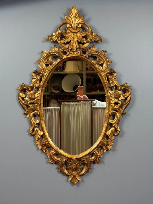 Miroir ovale vintage doré à la feuille d'or, cadre orné de motifs floraux rococo sculptés.